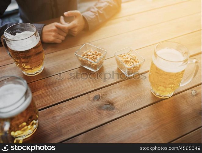 people, leisure and drinks concept - close up of male hands with beer mugs and peanuts at bar or pub