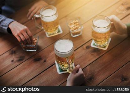 people, leisure and drinks concept - close up of male hands with beer mugs and peanuts at bar or pub