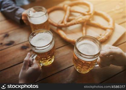 people, leisure and drinks concept - close up of male hands with beer mugs and pretzels at bar or pub