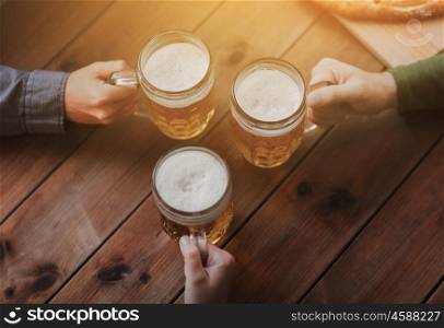 people, leisure and drinks concept - close up of male hands with beer mugs at bar or pub
