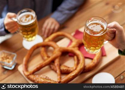 people, leisure and drinks concept - close up of male hands with beer mugs and pretzels on table at bar or pub