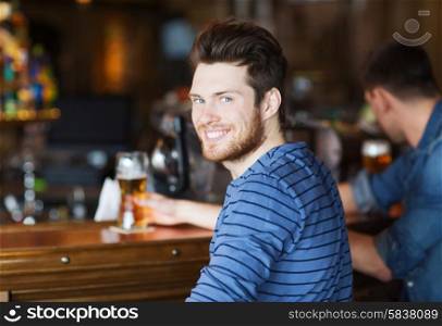 people, leisure and drinks concept - happy young man drinking beer at bar or pub