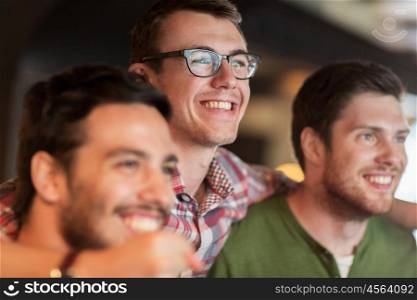 people, leisure and friendship concept - happy male friends watching sport game or football match at bar or pub