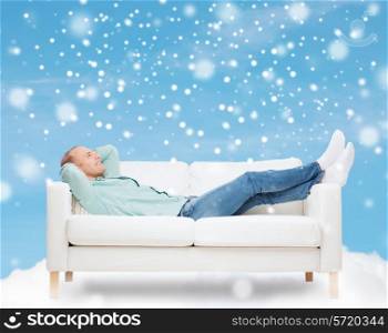 people, leisure and happiness concept - smiling man lying on sofa over blue sky with cloud and snow background