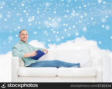 people, leisure and happiness concept - smiling man with book lying on sofa over blue sky with cloud and snow background