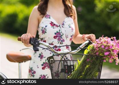 people, leisure and lifestyle concept - close up of young woman wearing summer dress with fixie bicycle and wild flowers in vintage basket at park. close up of woman with fixie bicycle in park
