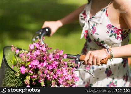 people, leisure and lifestyle concept - close up of young woman wearing summer dress riding fixie bicycle and wild flowers in vintage basket outdoors. close up of woman riding fixie bicycle outdoors