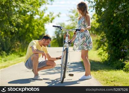 people, leisure and lifestyle concept - happy young couple fixing bicycle on country road in summer. happy young couple fixing bicycle on country road