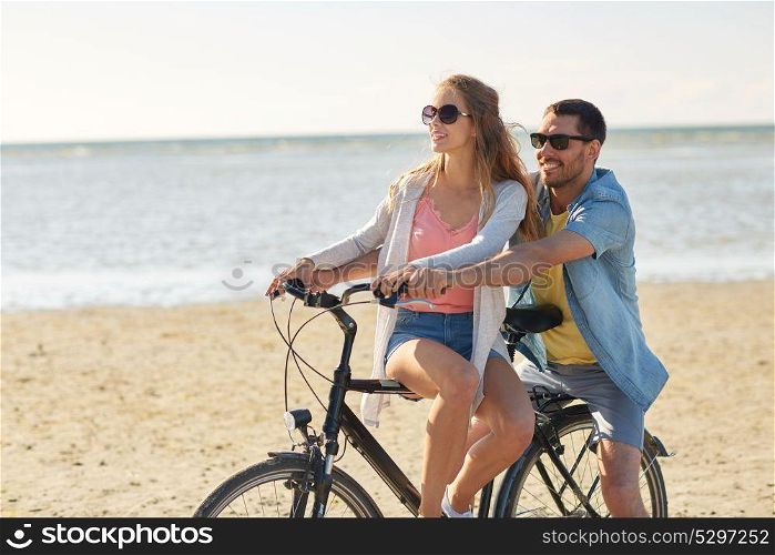 people, leisure and lifestyle concept - happy young couple riding bicycle on beach. happy young couple riding bicycle on beach