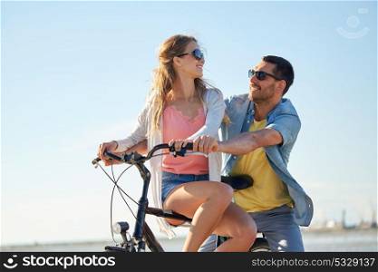 people, leisure and lifestyle concept - happy young couple riding bicycle on beach. happy young couple riding bicycle at seaside