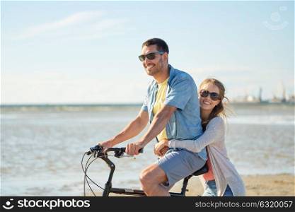 people, leisure and lifestyle concept - happy young couple riding bicycle on beach. happy young couple riding bicycle on beach