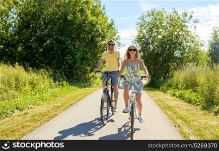 people, leisure and lifestyle concept - happy young couple riding bicycles along road in summer. happy young couple riding bicycles in summer