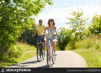 people, leisure and lifestyle concept - happy young couple riding bicycles along road in summer. happy young couple riding bicycles in summer