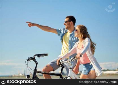 people, leisure and lifestyle concept - happy young couple riding bicycles at seaside. happy young couple riding bicycles at seaside