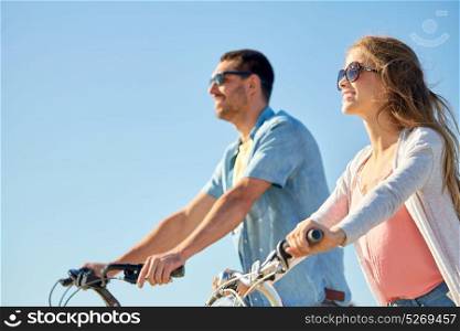 people, leisure and lifestyle concept - happy young couple riding bicycles in summer. happy young couple riding bicycles in summer