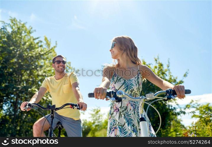 people, leisure and lifestyle concept - happy young couple riding bicycles in summer. happy young couple riding bicycles in summer