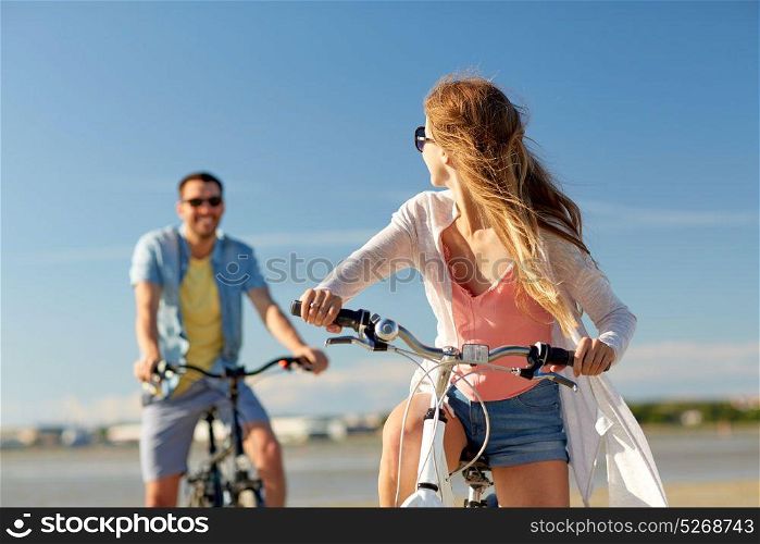 people, leisure and lifestyle concept - happy young couple riding bicycles on beach. happy young couple riding bicycles at seaside