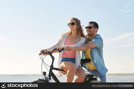 people, leisure and lifestyle concept - happy young couple riding bicycles on beach. happy young couple riding bicycles at seaside