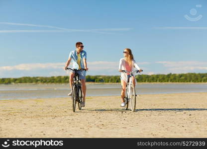 people, leisure and lifestyle concept - happy young couple riding bicycles on beach. happy young couple riding bicycles at seaside