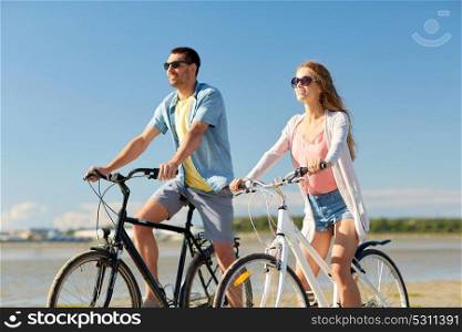 people, leisure and lifestyle concept - happy young couple riding bicycles on beach. happy young couple riding bicycles at seaside