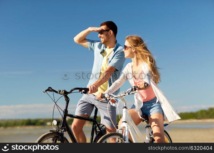 people, leisure and lifestyle concept - happy young couple riding bicycles on beach. happy young couple riding bicycles at seaside