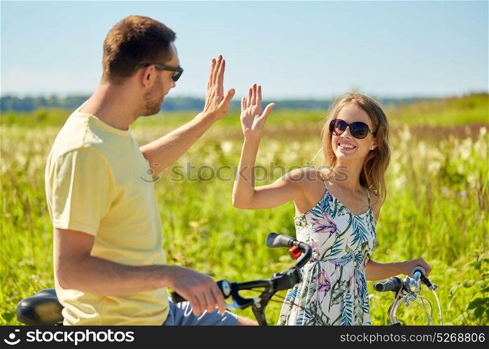 people, leisure and lifestyle concept - happy young couple with bicycles at country making high five. happy couple with bicycles making high five