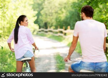 people, leisure and lifestyle concept - happy young couple with bicycles at summer park. happy couple with bicycles at summer park