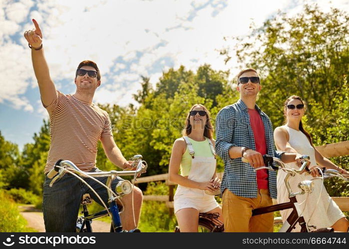 people, leisure and lifestyle concept - happy young friends riding fixed gear bicycles on country road in summer. happy friends riding fixed gear bicycles in summer