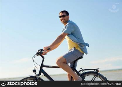 people, leisure and lifestyle concept - happy young man riding bicycle along summer beach. happy man riding bicycle along summer beach