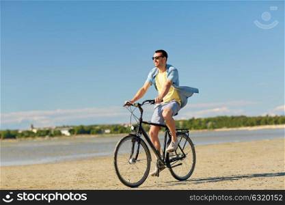 people, leisure and lifestyle concept - happy young man riding bicycle along summer beach. happy man riding bicycle along summer beach