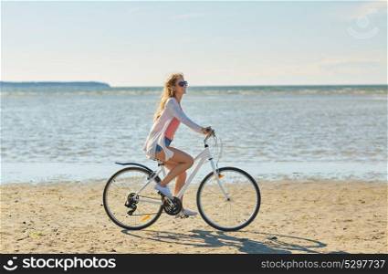people, leisure and lifestyle concept - happy young woman riding bicycle along summer beach. happy woman riding bicycle along summer beach