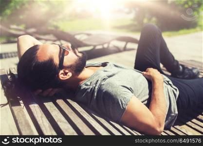 people, leisure and lifestyle - happy man lying on bench or sun bed on street. happy man lying on street bench or sun bed . happy man lying on street bench or sun bed