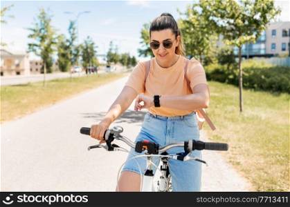 people, leisure and lifestyle - happy smiling young woman with smart watch riding bicycle on city street. woman with smart watch riding bicycle in city