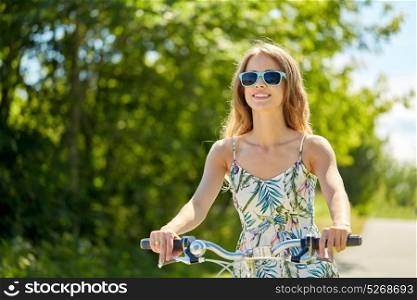 people, leisure and lifestyle - happy young hipster woman wearing summer dress and shades riding bicycle in summer. happy smiling young woman riding bicycle in summer