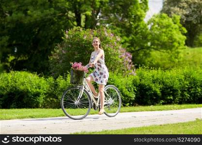 people, leisure and lifestyle - happy young hipster woman wearing summer dress riding fixie bicycle with wild flowers in basket at park. happy woman riding fixie bicycle in summer park