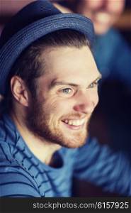 people, leisure and men concept - happy young man in hipster hat at bar or pub