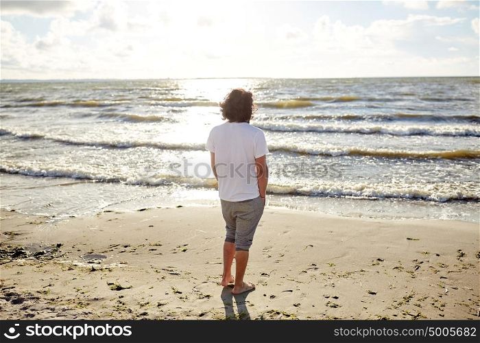 people, leisure and nature concept - young man on summer beach looking at sea. young man on summer beach looking at sea