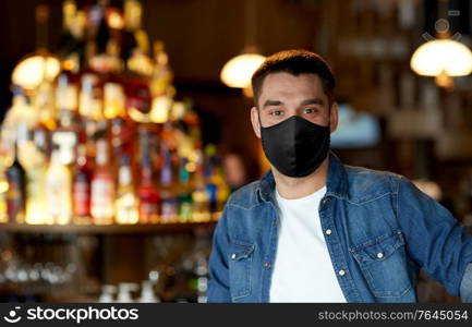 people, leisure and pandemic concept - young man wearing black reusable face protective mask for protection from virus disease at bar or pub. young man in black reusable mask at bar or pub