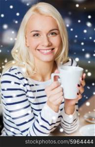 people, leisure and season concept - happy young woman drinking tea or coffee at winter cafe or home