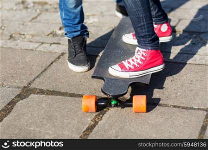 people, leisure and sport concept - close up of teenage couple feet with longboard on street