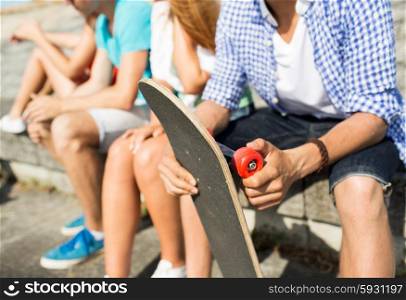 people, leisure and sport concept - close up of teenage friends with longboard talking on city street
