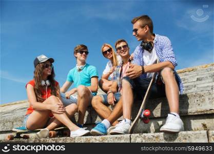 people, leisure and sport concept - group of happy teenage friends with longboard and headphones talking on city street