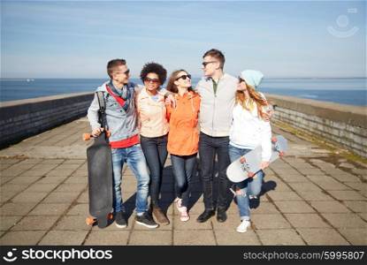 people, leisure and sport concept - group of happy teenage friends with longboards talking on city street