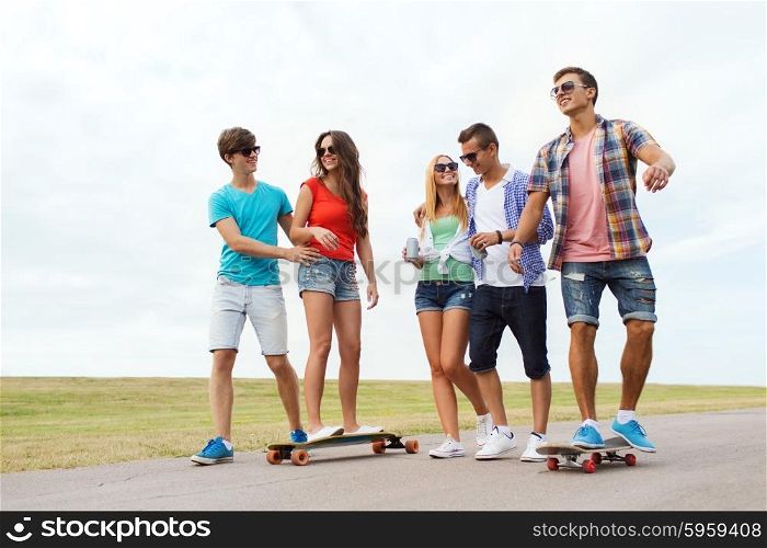 people, leisure and sport concept - group of happy teenage friends with longboards and drinks outdoors