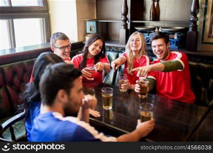 people, leisure and sport concept - happy friends or football fans drinking beer and watching soccer game or match at bar or pub, supporting two teams with different shirt color