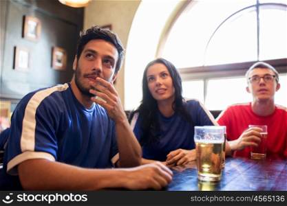people, leisure and sport concept - worried friends or football fans drinking beer and watching soccer game or match at bar or pub, supporting two teams with different shirt color