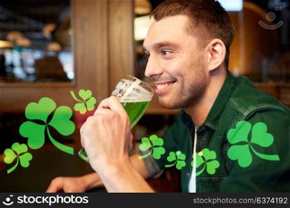 people, leisure and st patricks day concept - close up of happy young man drinking green beer at bar or pub. close up of man drinking green beer at bar or pub