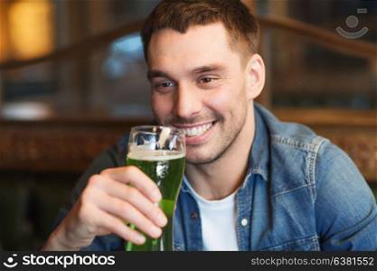 people, leisure and st patricks day concept - close up of happy young man drinking green beer at bar or pub. close up of man drinking green beer at bar or pub