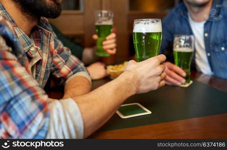 people, leisure and st patricks day concept - happy male friends drinking green beer at bar or pub. male friends drinking green beer at bar or pub