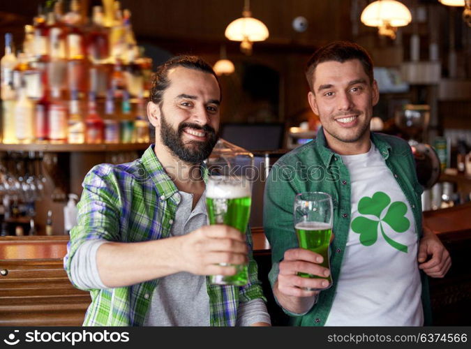 people, leisure and st patricks day concept - happy male friends drinking green beer at bar or pub. male friends drinking green beer at bar or pub